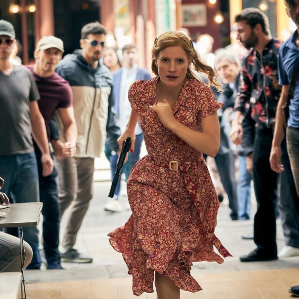 Jessica Chastain rennt in einem roten Kleid mit einer Waffe in der Hand durch eine Menschenmenge.