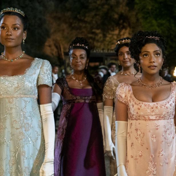 Frauen in Regency-Kleidern und Schmuck stehen bei einer formellen Veranstaltung.