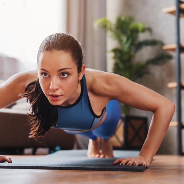 Eine Frau macht Liegestütze auf einer Yogamatte in einem Wohnzimmer.