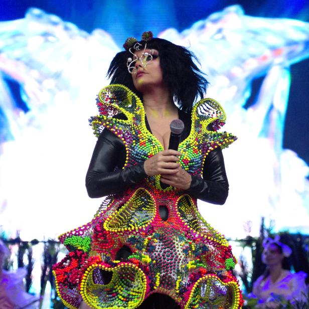 Björk tritt in einem farbenfrohen, extravaganten Kostüm auf einer Bühne auf.