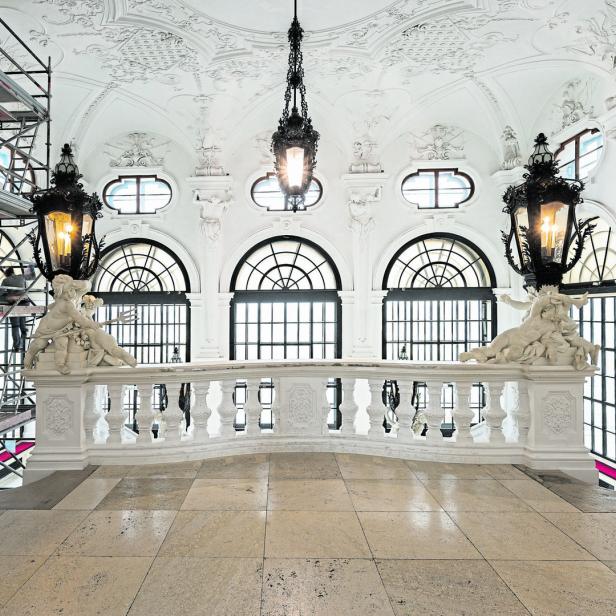Blick auf eine kunstvolle Balustrade mit Skulpturen in einem prunkvollen, weißen Saal.