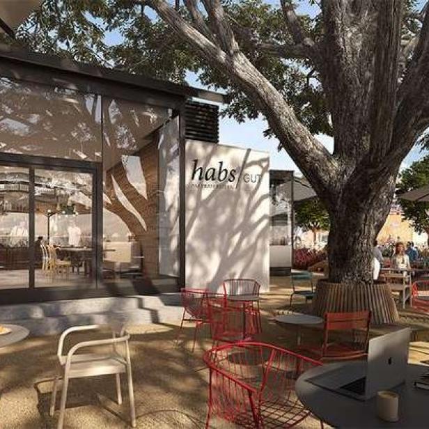 Ein Außenbereich des Restaurants „habs GU“ mit Gästen unter einem großen Baum.