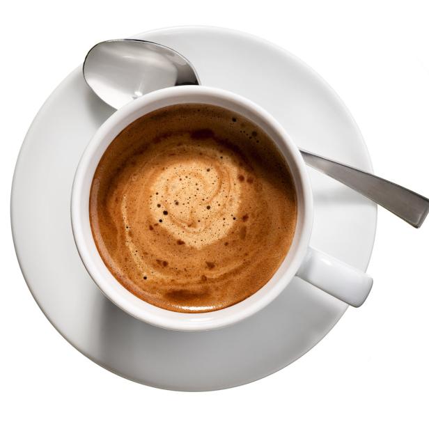 Eine Tasse Kaffee mit Milchschaum auf einer Untertasse mit einem Löffel.