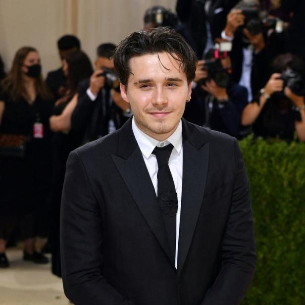 Brooklyn Beckham trägt einen schwarzen Anzug mit einer dunklen Krawatte und posiert für ein Foto.