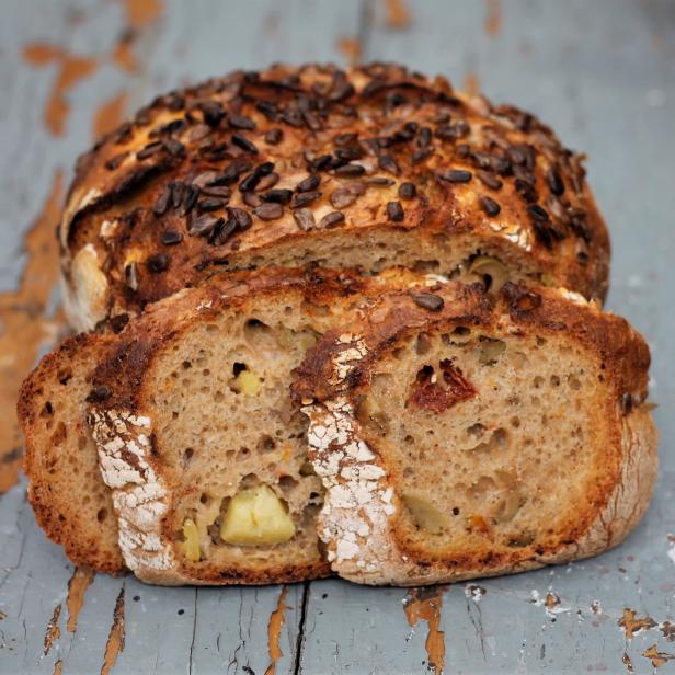 Ein angeschnittenes Brot mit Sonnenblumenkernen auf einer rustikalen Holzoberfläche.