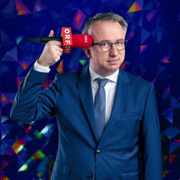 Ein Mann im Anzug hält ein rotes ORF-Mikrofon an seinen Kopf.
