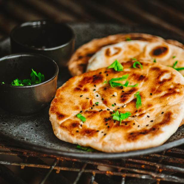 Auf einem Teller liegen Naan-Brote mit Kräutern und zwei Schälchen mit Dipsauce.