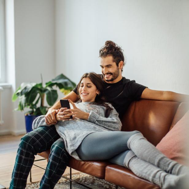 Ein Paar entspannt auf einem Ledersofa und schaut auf ein Smartphone.
