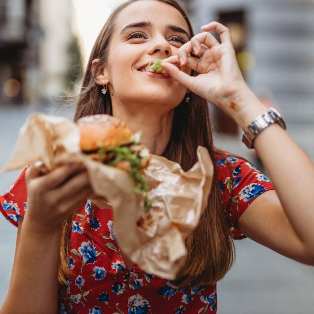 Eine junge Frau isst einen Burger auf der Straße.