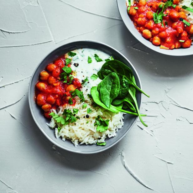Zwei Schalen mit Kichererbsen-Curry, Reis, Joghurt und Spinat auf einem Tisch.