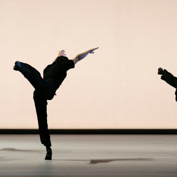 Drei Tänzer in schwarzen Kostümen führen eine synchrone Tanzroutine auf einer Bühne auf.