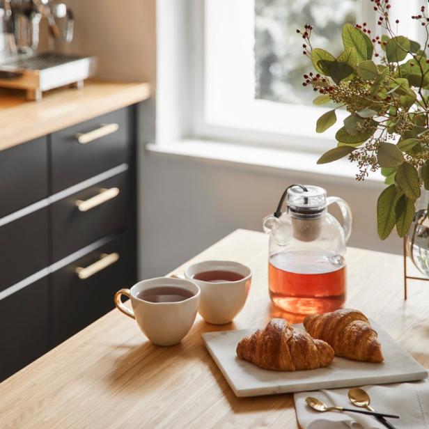 Zwei Croissants, zwei Tassen Tee und eine Teekanne auf einem Holztisch.