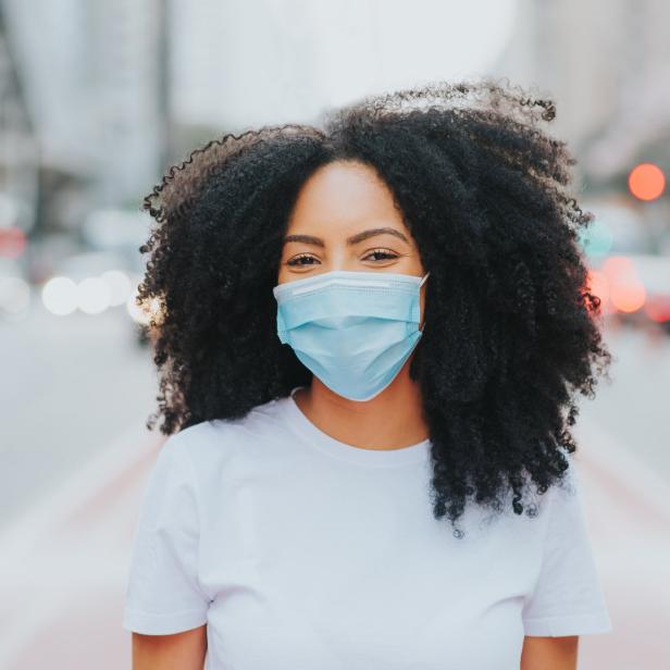 Eine Frau mit Afro-Haar und einer hellblauen Gesichtsmaske steht auf einer Straße.