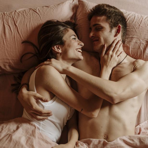 Ein lächelndes Paar liegt in einem rosa Bett und umarmt sich.