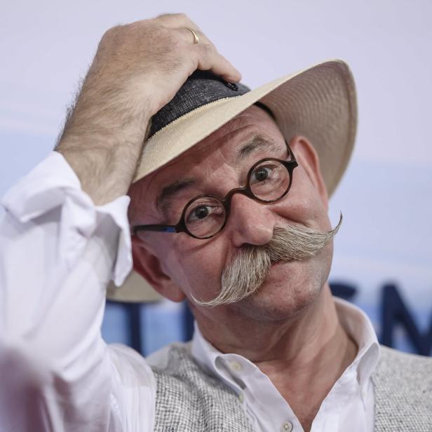 Ein Mann mit Hut, Brille und markantem Schnurrbart blickt in die Kamera.