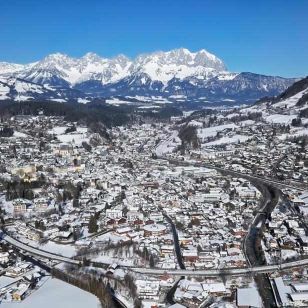 Ein verschneites Dorf liegt in einem Tal vor einer Bergkette.