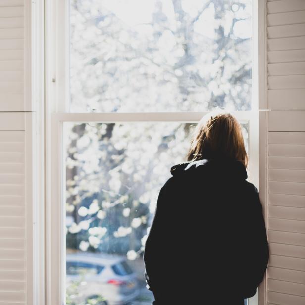 Eine Person blickt aus dem Fenster auf einen hellen, sonnigen Tag.