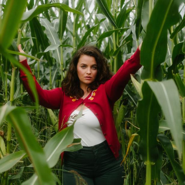 Eine Frau steht in einem Feld aus hohem, grünen Mais.