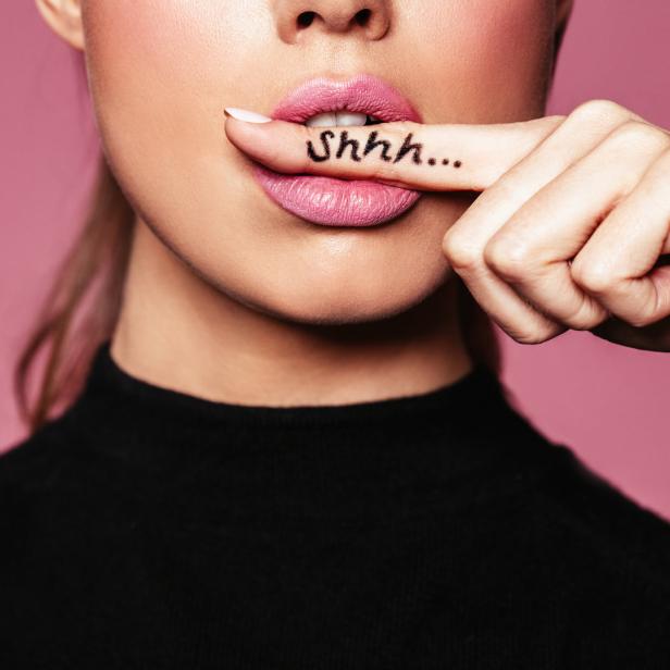 Eine Frau hält einen Finger mit der Aufschrift „Shhh…“ vor den Mund.