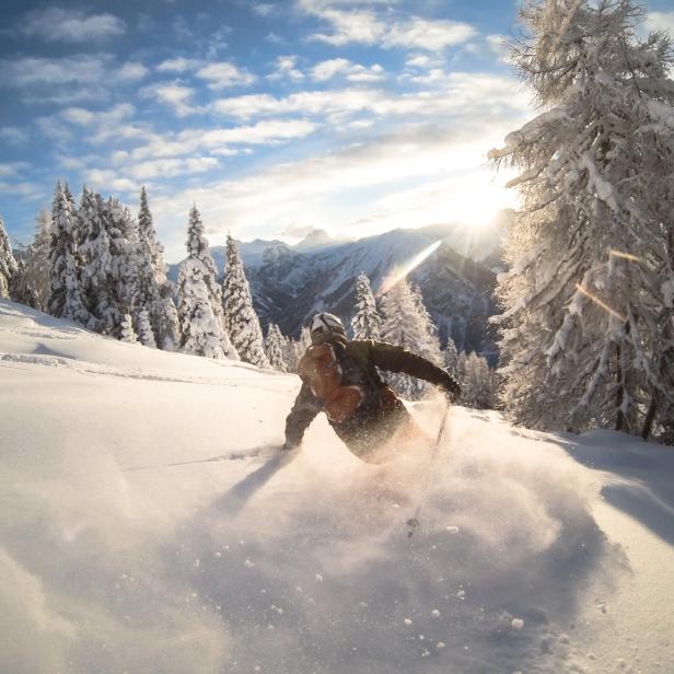 Ein Skifahrer fährt im Tiefschnee, umgeben von verschneiten Bäumen und Bergen.