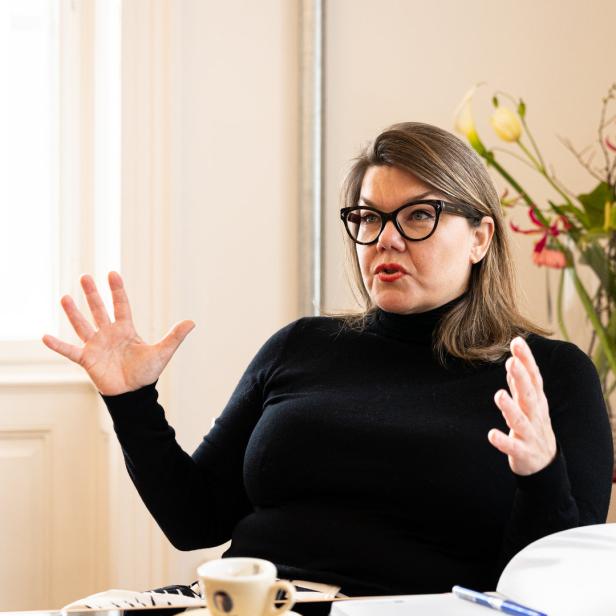 Eine Frau mit Brille gestikuliert während eines Gesprächs.