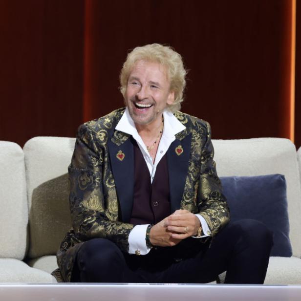Thomas Gottschalk sitzt lachend auf einem Sofa.