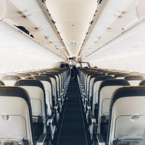 Blick in den Gang eines Flugzeugs mit Sitzen auf beiden Seiten.