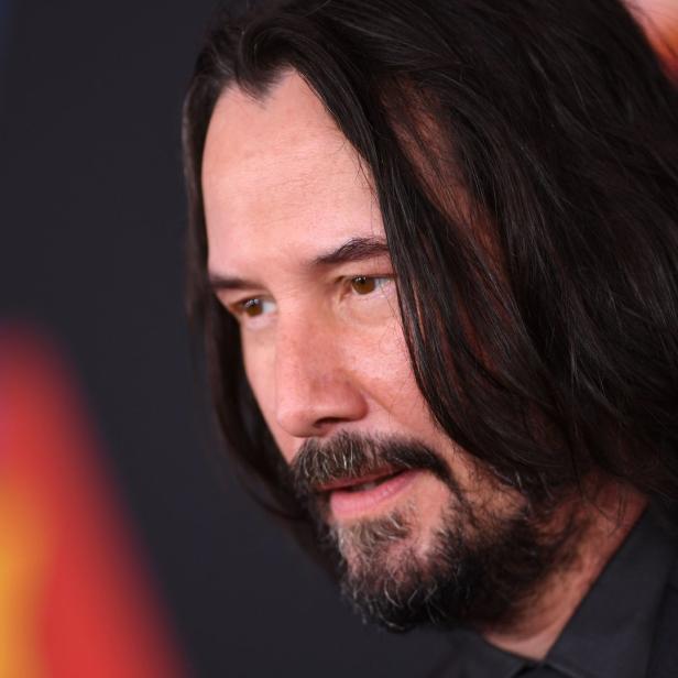 Nahaufnahme von Keanu Reeves mit Bart und langen, dunklen Haaren.