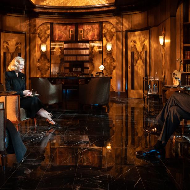 Cate Blanchett und Matt Bomer sitzen sich in einer eleganten Büroszene gegenüber.
