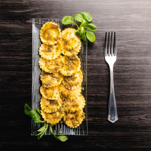 Eine rechteckige Glasplatte mit Ravioli und Pesto, daneben eine Gabel.
