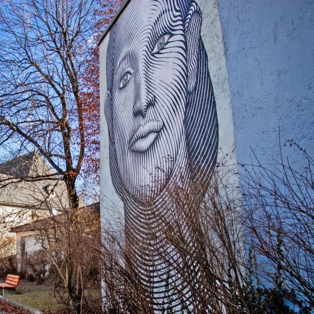 Ein großes Wandbild zeigt ein stilisiertes Frauengesicht neben einem Baum und einem Gebäude.