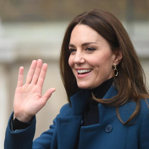 Kate Middleton lächelt und winkt in einem blauen Mantel.