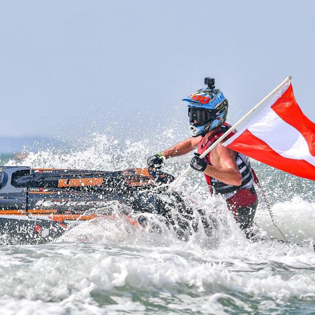 Ein Jet-Ski-Fahrer steht im Wasser und schwenkt eine rot-weiße Flagge.