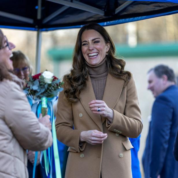 Kate Middleton lacht, während sie einen Blumenstrauß entgegennimmt.