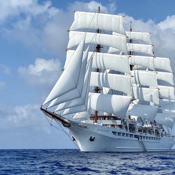 Ein großes Segelschiff mit weißen Segeln fährt auf dem offenen Meer.