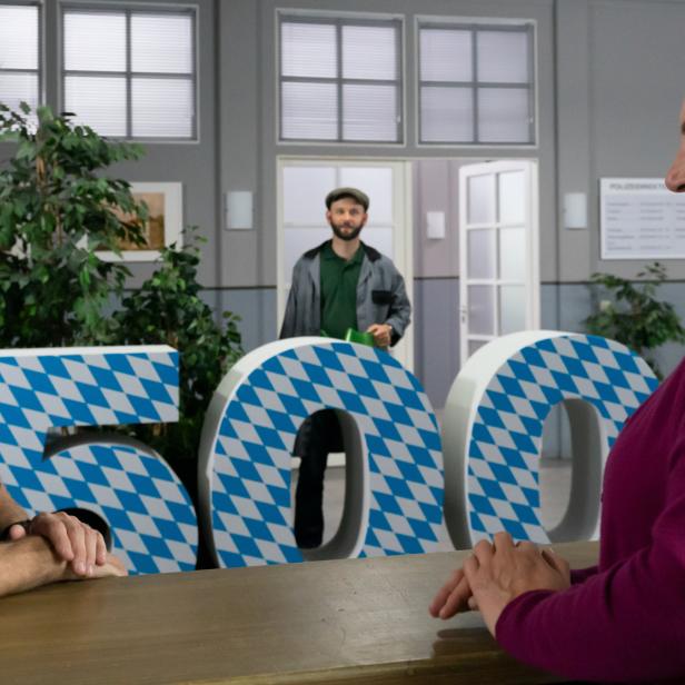 Ein Polizist spricht mit einer Frau vor großen, blau-weiß karierten Buchstaben.