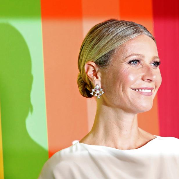 Gwyneth Paltrow mit hochgesteckten blonden Haaren und auffälligen Ohrringen vor einem bunten Hintergrund.
