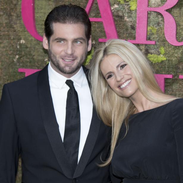 Michelle Hunziker und ein Mann posieren vor einer Wand mit pinkfarbenen Buchstaben.