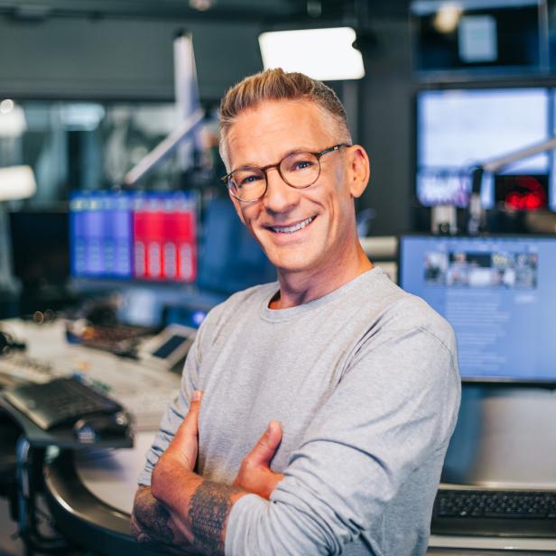 Ein Mann mit Brille lächelt in einem Radiostudio in die Kamera.