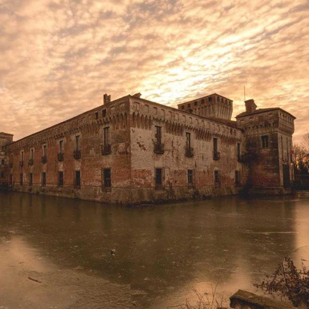 Ein altes Backsteinschloss ist von einem trüben Wassergraben umgeben.