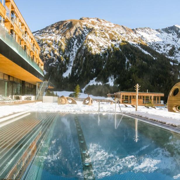 Ein Außenpool mit Blick auf schneebedeckte Berge an einem sonnigen Tag.