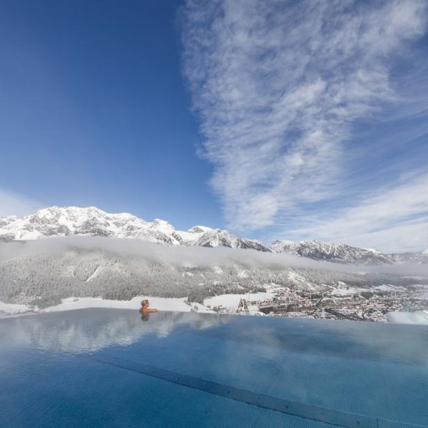 Eine Frau entspannt in einem Infinity-Pool mit Blick auf schneebedeckte Berge.