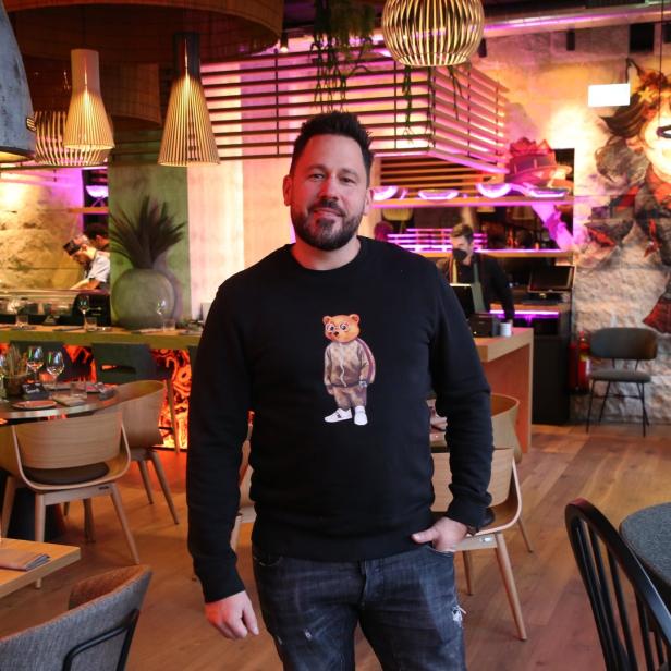 Ein Mann mit einem Bären-Sweatshirt steht in einem modern eingerichteten Restaurant.