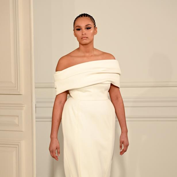Eine Frau präsentiert ein schulterfreies, weißes Kleid auf einem Laufsteg.
