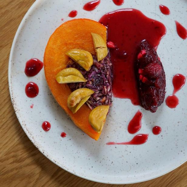 Ein Teller mit Kürbis, Rotkohl, Pflaumen und roter Sauce.