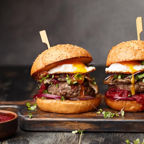 Zwei Burger mit Spiegelei, Pilzen und roter Zwiebel auf einem Holzbrett.