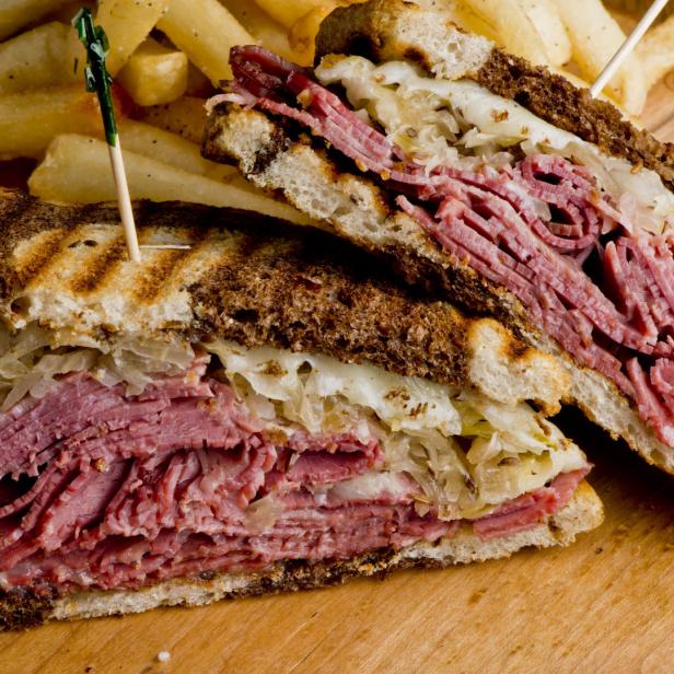 Ein aufgeschnittenes Reuben-Sandwich mit Pommes Frites auf einem Holzbrett.