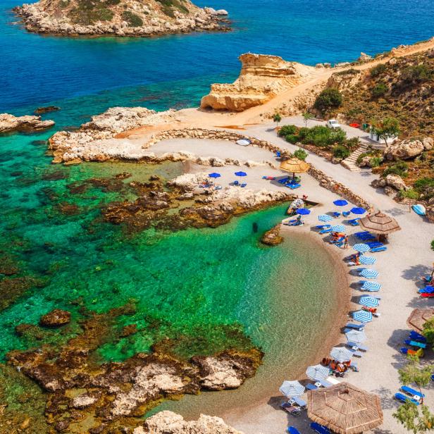 Ein Strand mit türkisfarbenem Wasser und vielen Sonnenschirmen.