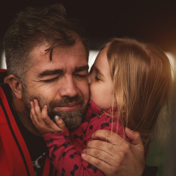 Ein kleines Mädchen gibt ihrem Vater einen Kuss auf die Wange.