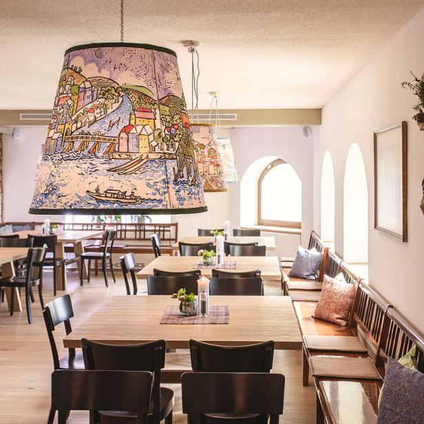 Ein Speisesaal mit Holztischen, Stühlen und Lampen mit Flusslandschaftsmotiven.